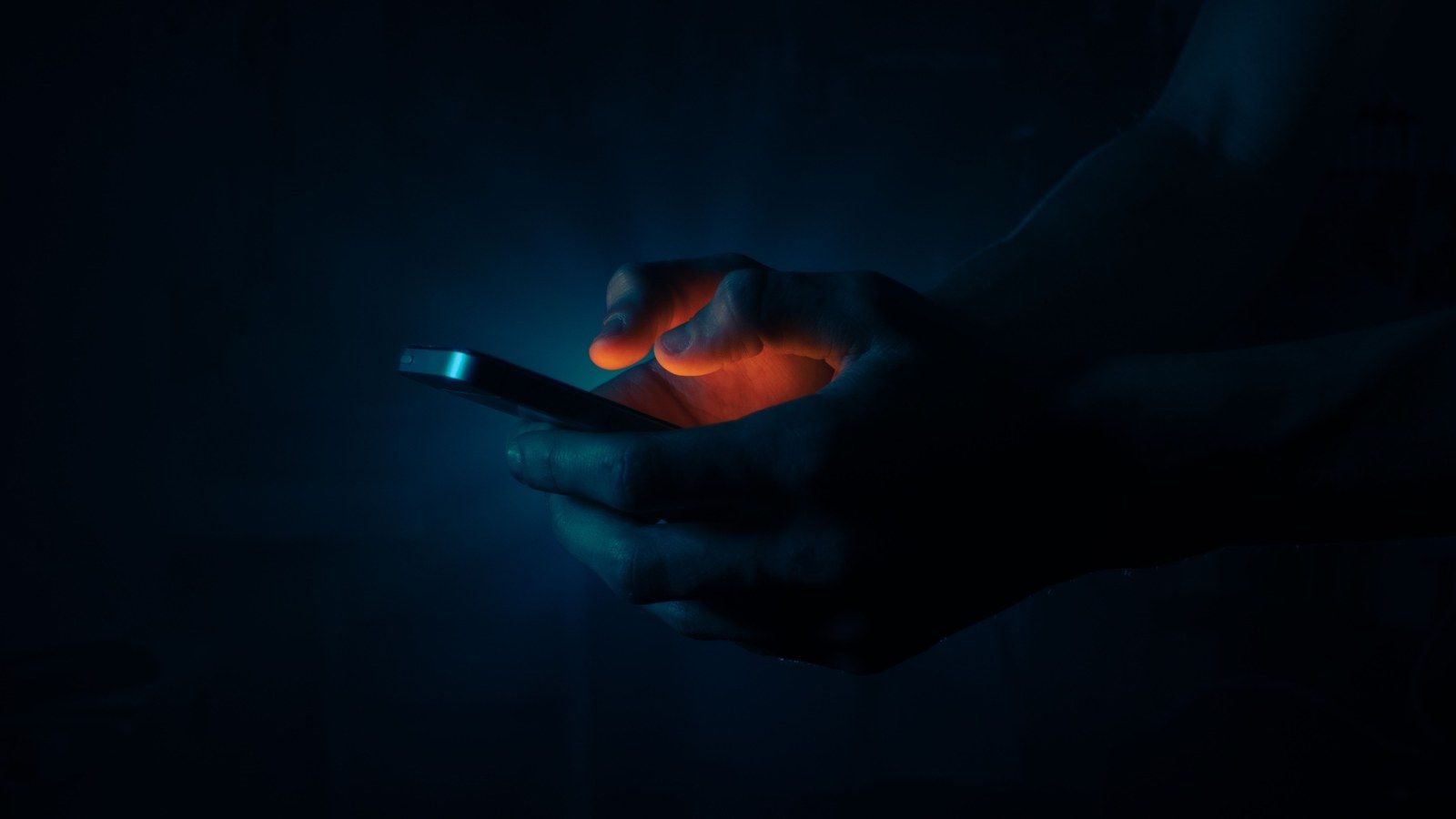 Stock photo of hands holding a glowing phone in the dark, illustrative only, no identifiable person shown