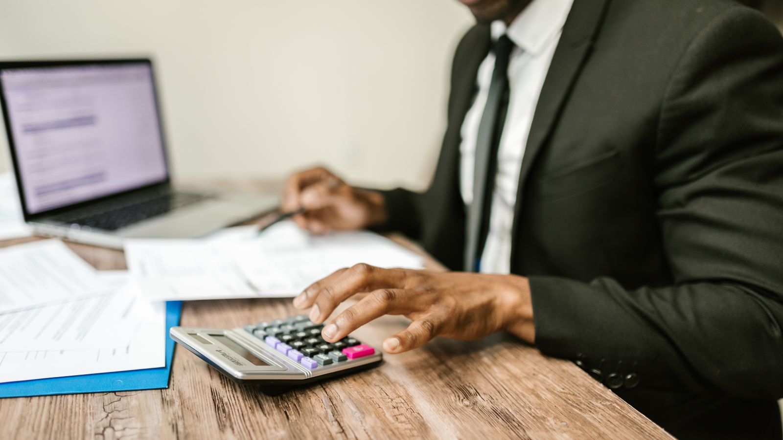 Stock photo of a person in a suit using a calculator and laptop at a desk, illustrative only, not Rillet's actual product or team